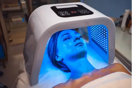 Client receiving blue LED light therapy under a facial treatment lamp.