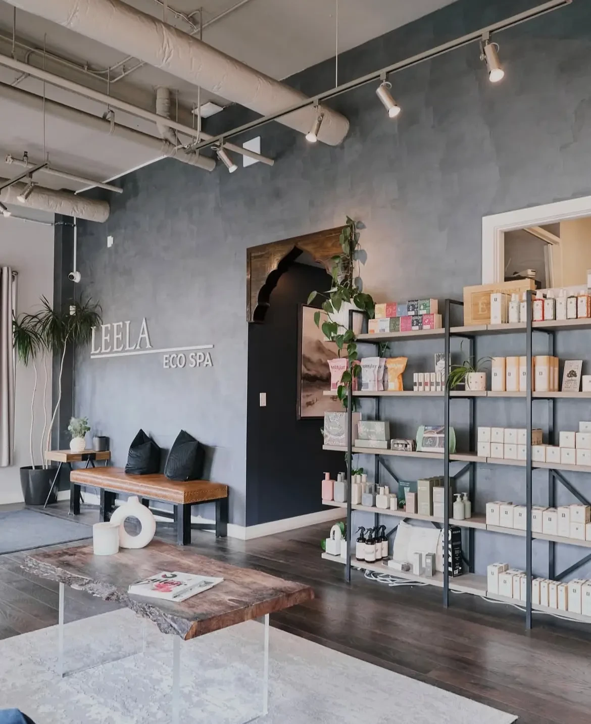 Reception lounge at Leela Eco Spa Bridgeland — LEELA ECO SPA wall lettering, live-edge table, and retail shelving.