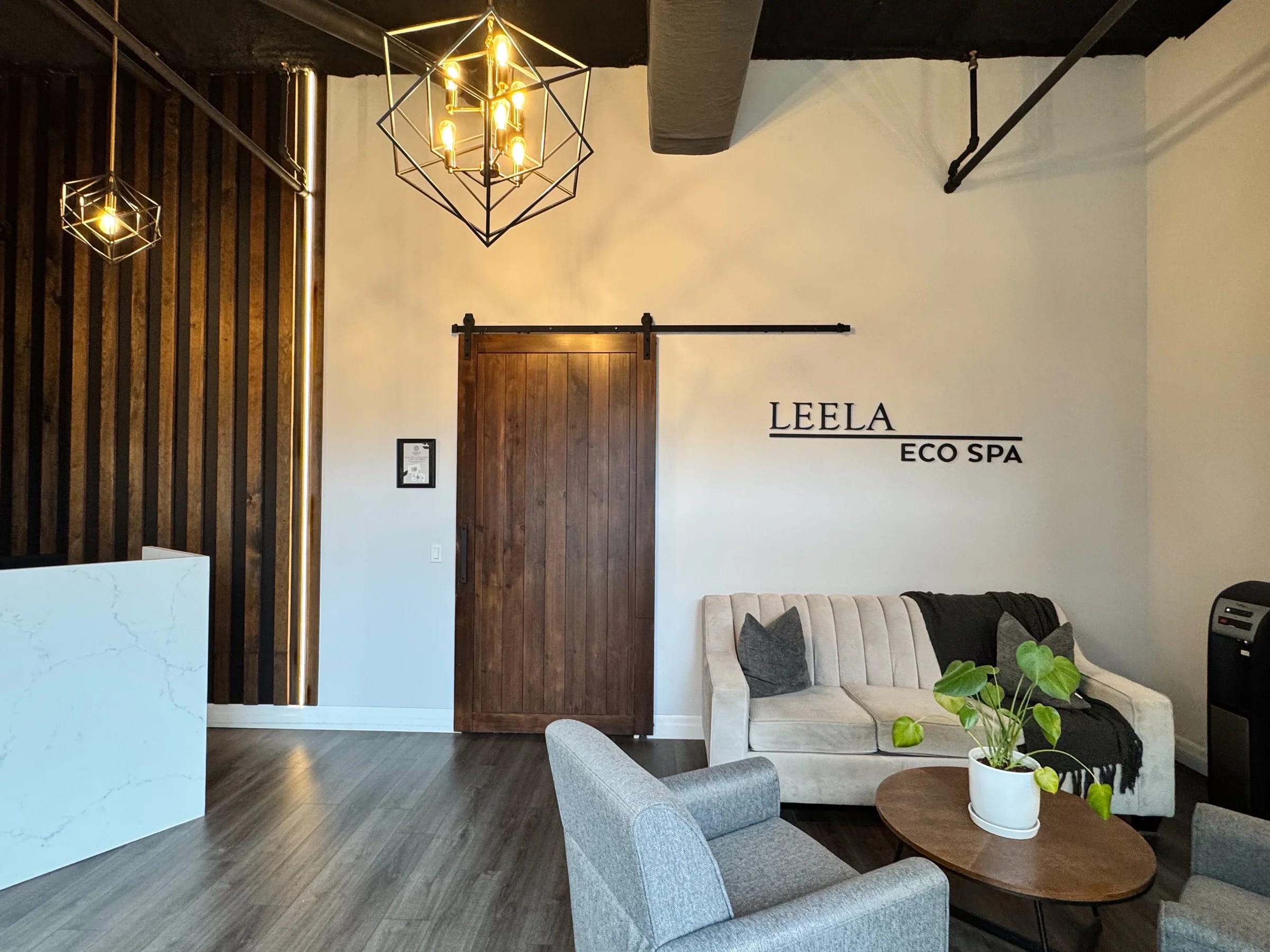 Reception lounge at Leela Eco Spa Town Square in Oakville, with pendant lights, a wooden sliding door, and comfortable seating beneath the Leela Eco Spa sign.