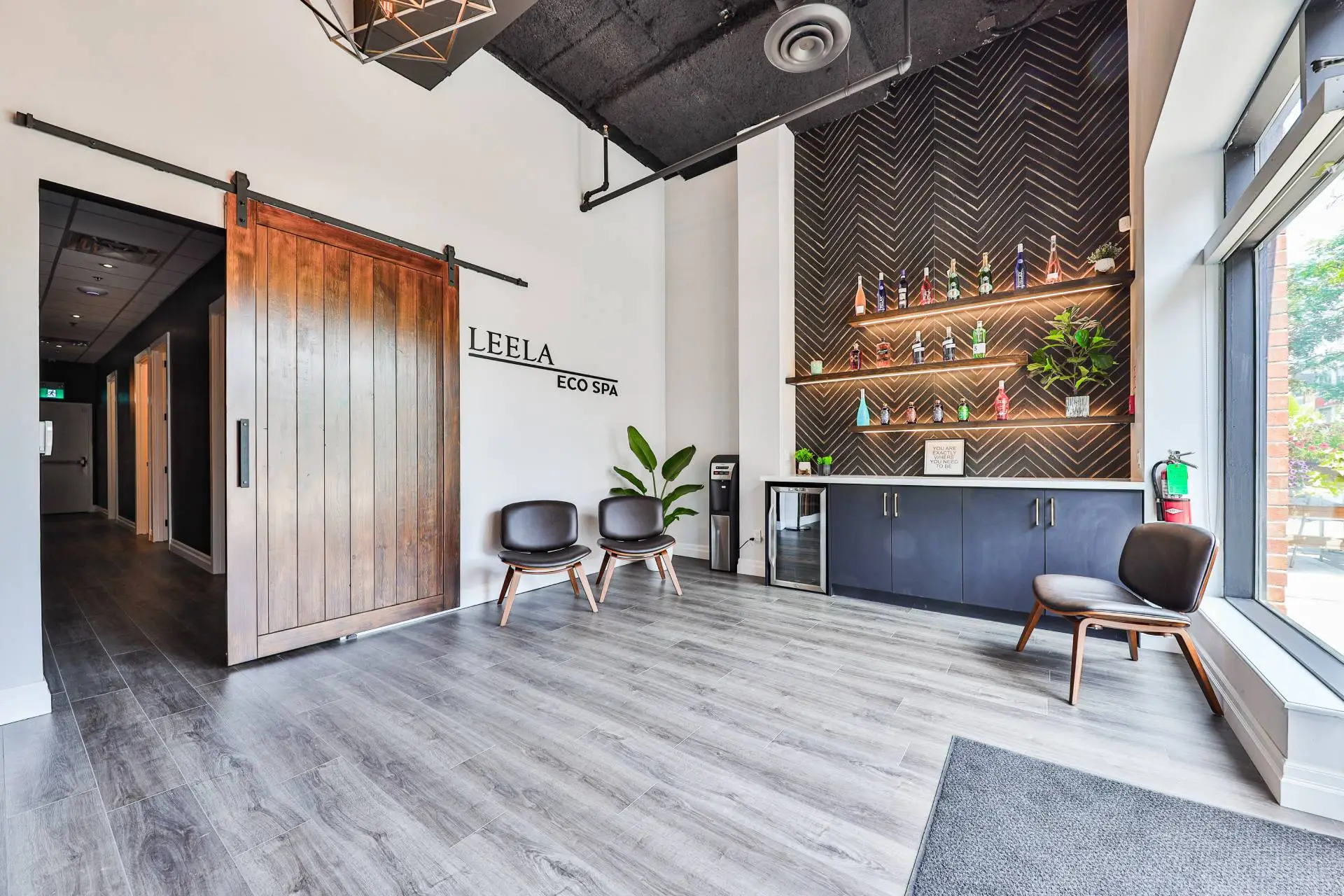Reception at Leela Eco Spa Town Square massage studio in Oakville, with a wood-slat wall and waiting chairs.
